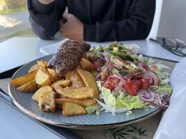 Kebab with French fries and salad on a plate on white table in a restaurant photo