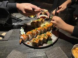 Unrecognized man and unrecognized little girl hand's using chopsticks to pick up pieces of sushi from a large platter, which includes various types of rolls and nigiri. photo