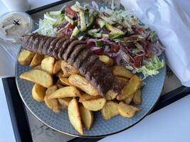 A plate of Kebab with French fries and salad on a rustic plate in a restaurant. Close up view photo