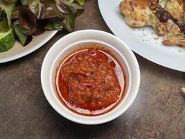 Delicious Indonesian tomato sambal in a white bowl and fried thighs with vegetables photo