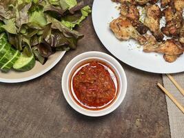 Delicious Indonesian sambal in a white bowl and fried thighs with vegetables. Close up photo