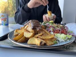 Unrecognized man enjoying Kebab with French fries and salad on a plate on white table in a restaurant photo