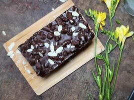 A decadent chocolate cake with almonds and chocolate chips. Yellow freesias nearby. photo
