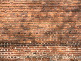 A wall constructed entirely of red brick with variation in color and texture throughout in a traditional pattern, with visible mortar joints that create a grid-like effect with tree shadow on it. photo