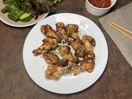 Fried chicken thighs sprinkled with onions and parsley on a white plate served with tomato sauce, cucumber and lettuce photo