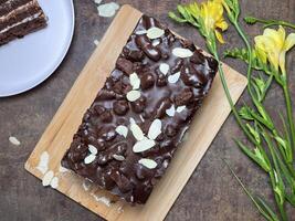 A decadent chocolate cake with almonds and chocolate chips. A slice rests on a pink plate. Yellow freesias nearby. photo