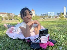 Smiling Asian little girl on the grass using phone in outdoor making call with love sign hand gesture photo