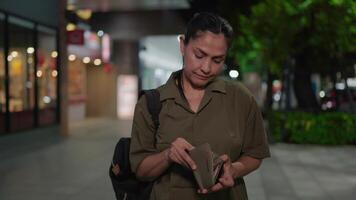 A middle-aged woman examines her empty wallet at night, her bored expression turning to disappointment as she looks up and rubs her stomach softly, showcasing the emotions tied to hunger video