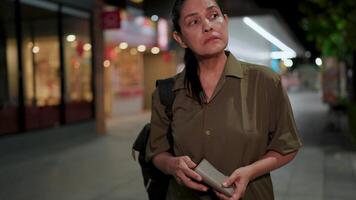 Woman looks around with a disappointed expression while checking her empty wallet, reflecting on her financial struggles amid the dimly lit atmosphere of the city video