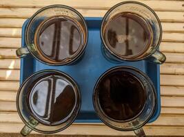 Top-down view of four cups filled with black coffee placed on a blue tray. The reflective surface of the coffee contrasts with the transparent glass mugs. . photo