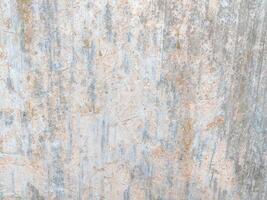 Weathered surface with vertical streaks and faded spots in light gray and beige tones. The textured wall showcases signs of aging, roughness, and subtle color variations in an abstract pattern. photo