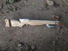 A handcrafted wooden crossbow with a visible string and trigger mechanism, lying on a dirt ground. The crossbow has a rustic, homemade appearance. photo