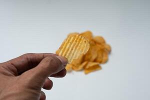 A hand holding a ruffled potato chip The chip is being held up to show off the ripples and it s a bit broken off photo