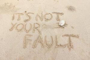 Motivation quotes It is not Your Fault written in the sand of the beach photo