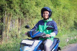 Online taxi rider wearing green jacket and helmet, riding motorcycle while on the way to pick up customer. Transportation application concept. photo