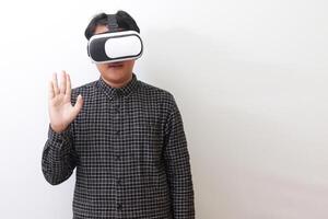 Portrait of Asian man in black plaid shirt using Virtual Reality VR glasses and greet his friend inside the game with opened palm. Isolated image on white background photo