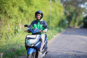 Online taxi rider wearing green jacket and helmet, riding motorcycle while on the way to pick up customer. Transportation application concept. photo
