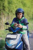 Online taxi rider wearing green jacket and helmet, riding motorcycle, using a mobile phone while on the way to pick up customer. Transportation application concept. photo