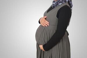 Cropped portrait of unrecognizable pregnant muslim woman with hands over tummy. Isolated image on white background photo