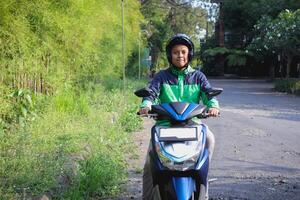 Online taxi rider wearing green jacket and helmet, riding motorcycle while on the way to pick up customer. Transportation application concept. photo