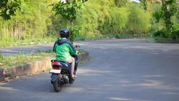 Back view of online taxi rider wearing green jacket and helmet, riding motorcycle while on the way to pick up customer. Transportation application concept. photo