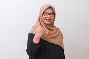 Portrait of cheerful Asian woman with hijab, showing product, pointing at something and smiling. Advertising concept. Isolated image on white background photo