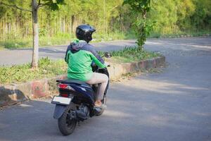 Back view of online taxi rider wearing green jacket and helmet, riding motorcycle while on the way to pick up customer. Transportation application concept. photo