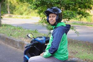 Back view of online taxi rider wearing green jacket and helmet, riding motorcycle while on the way to pick up customer. Transportation application concept. photo
