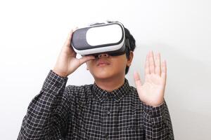 Portrait of Asian man in black plaid shirt using Virtual Reality VR glasses and greet his friend inside the game with opened palm. Isolated image on white background photo