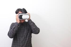 Portrait of Asian man in black plaid shirt using Virtual Reality VR glasses and looking up. Isolated image on white background photo