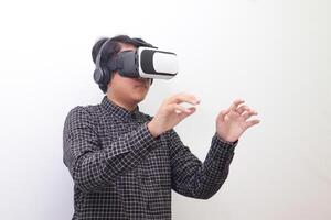 Portrait of Asian man in black plaid shirt using Virtual Reality VR glasses and trying to hold something in front of him. Isolated image on white background photo