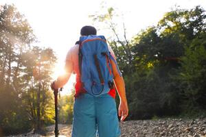 Man hiking with backpac and sticks in mountains in sunset photo