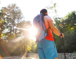 Man hiking with backpac and sticks in mountains in sunset photo