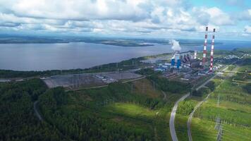 Top view of power plant on lake shore. Clip. Factory pipes on background of lake and green forest. Landscape with power station and pipes by lake in summer video