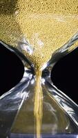 Close-up of golden hourglass. Stock footage. Stylish hexagon hourglass with falling gold specks on black isolated background. Passage of time and importance of every grain video