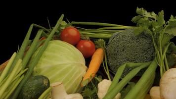 A wooden crate filled with fresh vegetables. The crate contains a variety of colorful produce, including tomatoes, green peppers, yellow peppers, cabbage, cucumbers, scallions, and corn. video