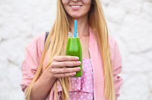 Healthy woman posing with fresh juice bottle of green detox smoothie photo