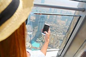 Girl tourist with mobile phone by the window of skyscraper of the Burj Khalifa in Dubai, United Arab Emirates photo