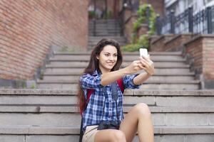 Portrait of a young attractive woman holding a smartphone digital camera with her hands and taking a selfie self portrait of herself photo
