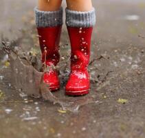 Child wearing red rain boots jumping into a puddle photo