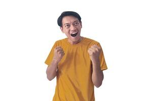 Handsome Asian man in a orange shirt raises both fists in a celebratory gesture, his face beaming with excitement and on white background emphasizes his triumphant and enthusiastic expression. photo