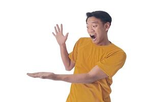 Portrait of an Asian man wearing a orange T-shirt, expressing surprise and shock with open palms, isolated against a white background. photo