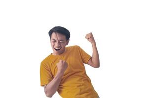 Handsome Asian man in a orange shirt raises both fists in a celebratory gesture, his face beaming with excitement and on white background emphasizes his triumphant and enthusiastic expression. photo