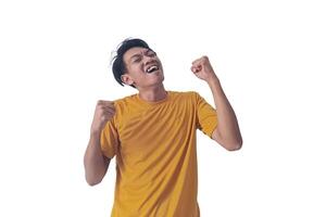 Handsome Asian man in a orange shirt raises both fists in a celebratory gesture, his face beaming with excitement and on white background emphasizes his triumphant and enthusiastic expression. photo