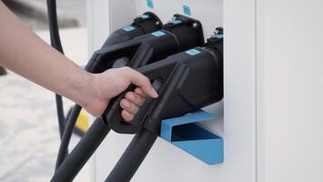 Hand holding EV charging plug in front of camera with blurred background of outdoor. Driver of electric car hold batteries charger plug. Sustainable energy powered electric charging station background photo
