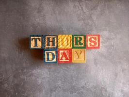 A photo of a wooden block with the words thursday written on it, styled in isolation with space for text.