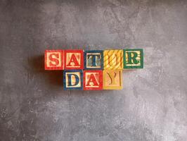A photo of a wooden block with the words saturday written on it, styled in isolation with space for text.