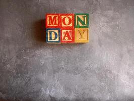 A photo of a wooden block with the words monday written on it, styled in isolation with space for text.