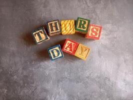 A photo of a wooden block with the words thursday written on it, styled in isolation with space for text.