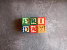 A photo of a wooden block with the words friday written on it, styled in isolation with space for text.